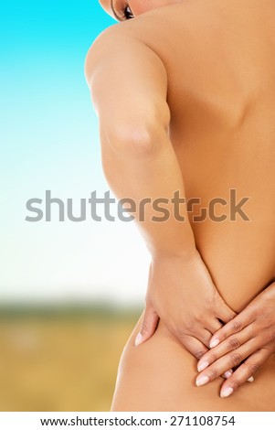 Naked woman touching her lower back.