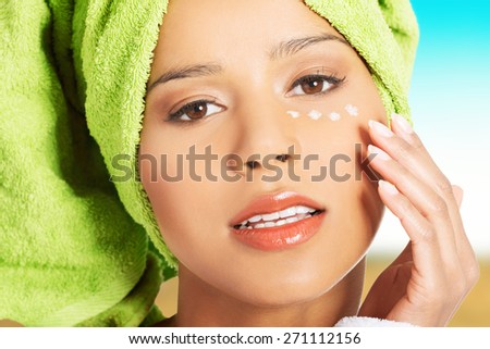 Woman in bathrobe and turban with eye cream.