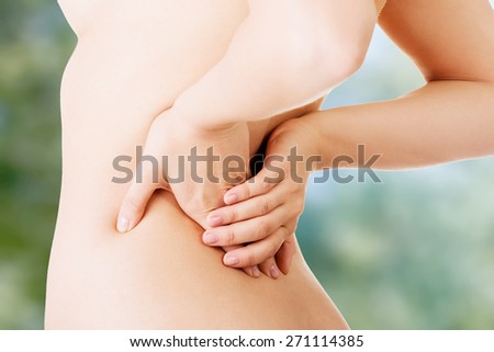 Naked woman touching her lower back.