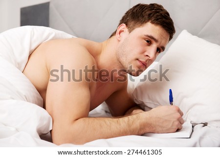 Handsome man writing a note in his bedroom on bed.