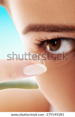 Woman applying contact lens in her eye.