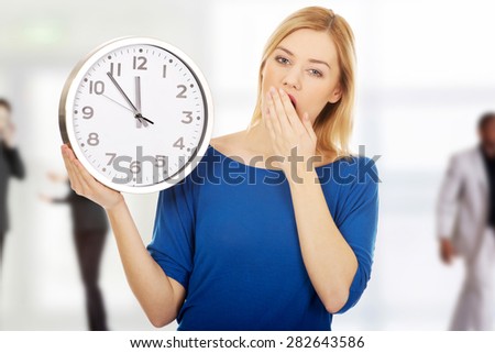 Young yawning woman holding a clock.