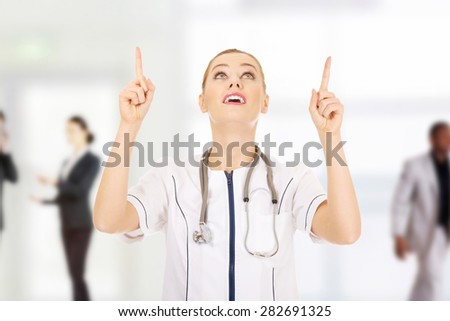 Smiling medical doctor woman pointing up.