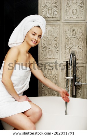 Beautiful woman pours water in a bath.
