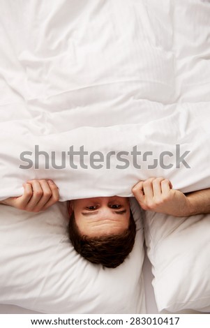 Funny man hiding in bed under the sheets.