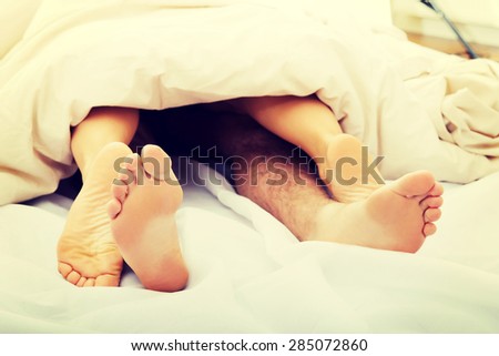 Couple\'s feet in bed under the quilt.