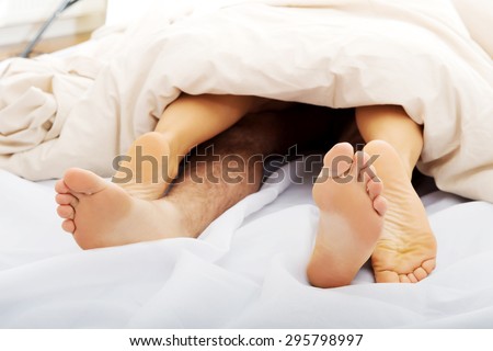 Couple's feet in bed under the quilt.