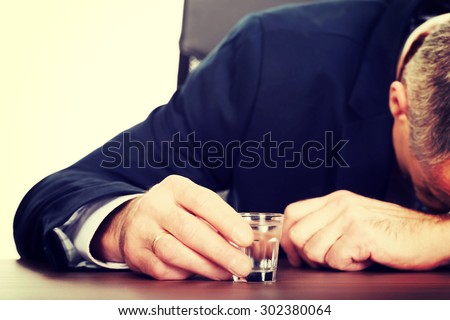Overworked mature man drinking vodka in office.
