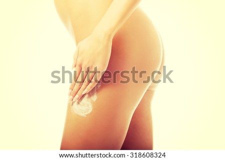 Spa undressed woman applying cream on thigh.