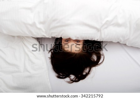 Scared woman hiding behind sheet in bed.
