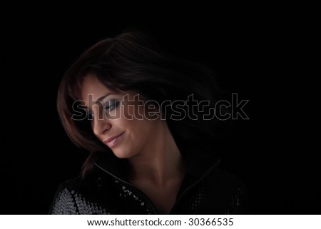 Beautiful young woman with long healthy dark hair on dark black background.