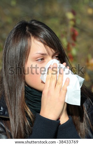 Teen Girl blowing her nose outdoors in late autumn.