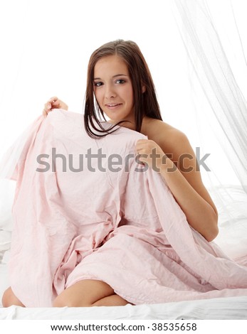Yong brunette sitting on the bed and covering her naked body with pink bed sheet
