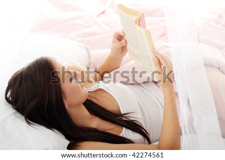 Sensual young woman laying in pink bed. Reading