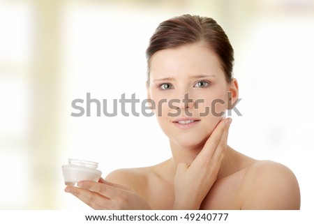 Woman applying moisturizer cream on face. Close-up on woman face.