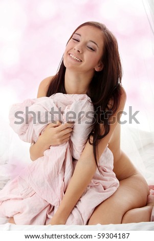 Young brunette sitting on the bed and covering her naked body with pink bed sheet
