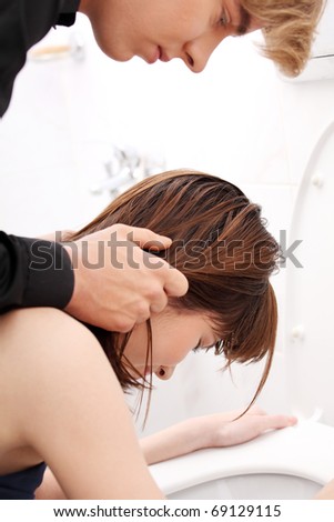 Boy holding his girlfriend head above toilet.