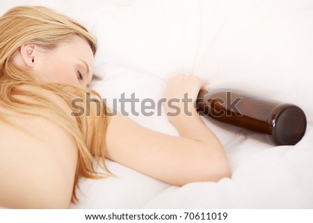 Drunk young topless woman sleeping on bed with bottle of vine in hand. Isolated on white