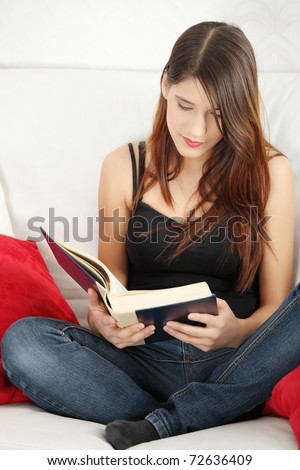 Beautiful woman reading a book, sitting on a sofa in a living-room