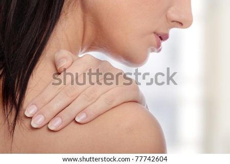Woman from behind, naked body, holding her neck on the left side. Horizontal.