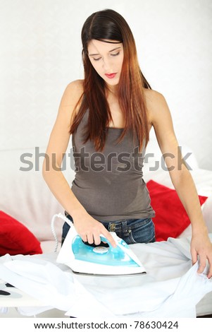 Happy young woman ironing her shirt on ironing board