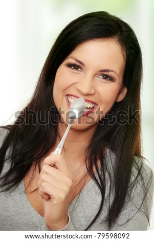 Portrait of young smiling woman with spoon in her mouth and (pleasure from eating).