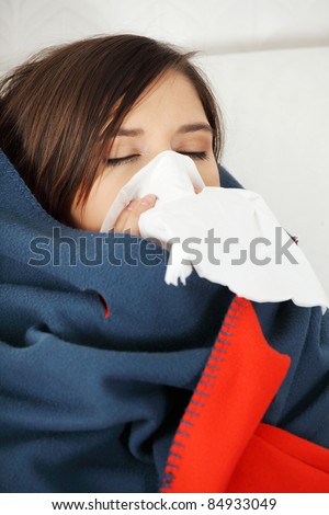 Young woman at home having flu, wrapped up in blanket, sneezing.