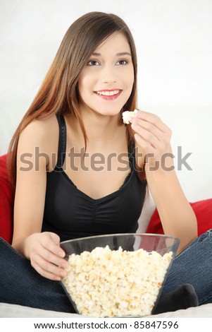Beautiful young woman watching TV and eating popcorn