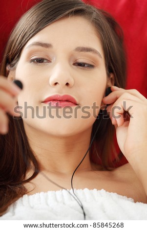 Listening to music. Young woman relaxing at home after bath, listening to music, lying on sofa in towel.