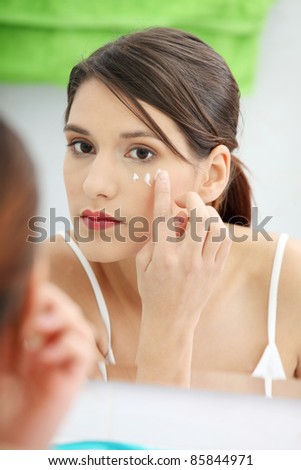 Beautiful woman applying cream on face at bathroom