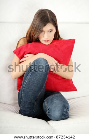 Sad woman\'s sitting on couch and squeezing pillow.