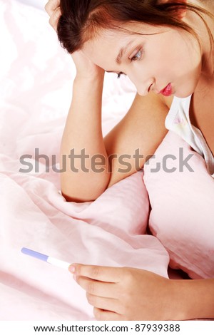 Teen pretty depressed girl checking her pregnant test in bed.
