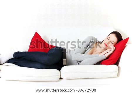 Front view portrait of a young beautiful woman lying on a sofa, being hugged to a red pillow, holding her hands close to the face.