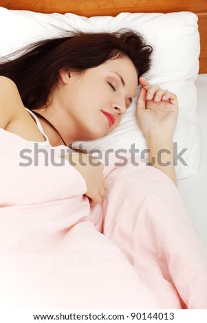 Site view closeup of a young beautiful woman sleeping in the bed, resting her left hand next to her face.