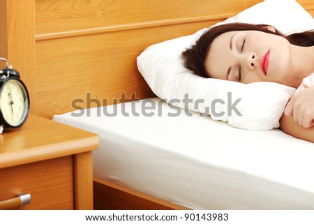 Face closeup of a young beautiful woman sleeping in bed, with a black alarm clock in the left site of the picture.