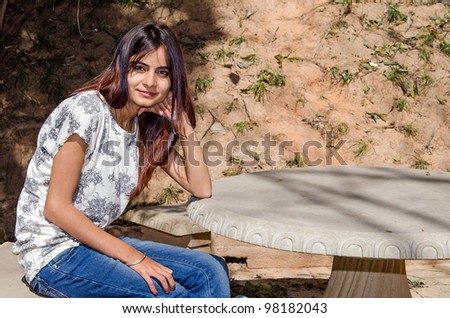 Young beautiful girl sitting on a stone bench leaning on a stone table in park.