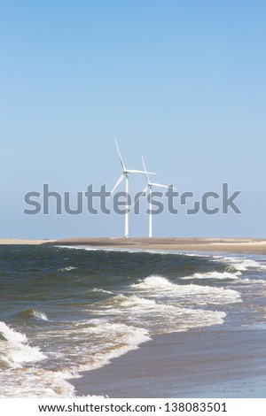 Two wind turbines on the horizon of a beach where the waves of the sea roll on.
