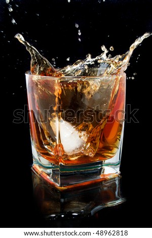 Whiskey splash. Glass with reflection against black background.