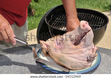 A man prepares to roast a pig head on a charcoal grill for a backyard party