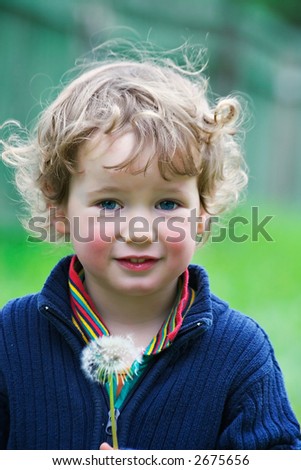 Boy with curly hair holds a dandelion in hands
