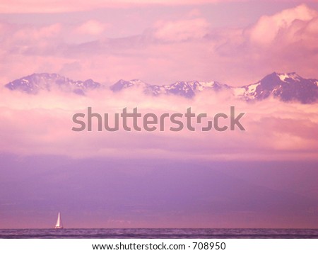 Sailboat on the ocean at sunset with mountains peeking through the clouds