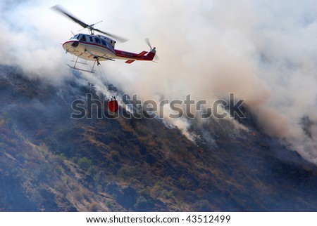 fire-fighting helicopter with a water bucket fighting a fire on a hillside