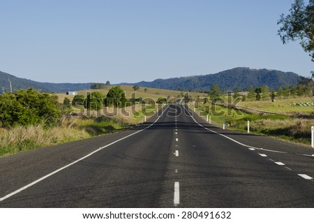 Rural asphalt road in Queensland, Australia. White road marking lines in middle of road. Farmlands on either side of road. No clouds on sky.