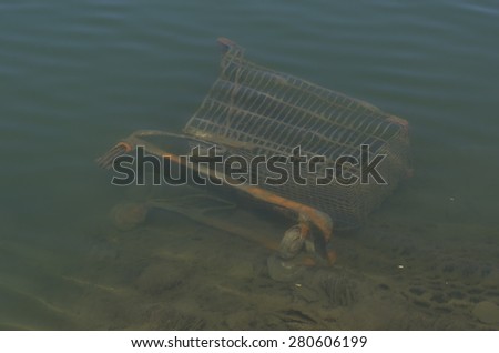 Dumped shopping trolley in submerged in water on its side. Brown algae is growing on shopping trolley indicating that it\'s been under water for a while. Slight ripples on water surface.