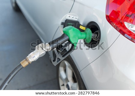 Petrol pump nozzle placed in silver car\'s petrol tank ready to fill up. Shallow focus on nozzle. Image shows part of car\'s tail light. Petrol nozzle head is green plastic.