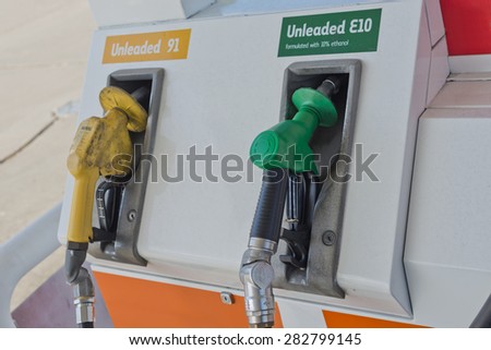 Image of a couple of petrol fuel pump nozzles on the pump at petrol station. One is unleaded E10 and has a green nozzle while the other is Unleaded 91 and has a yellow and dirty nozzle.