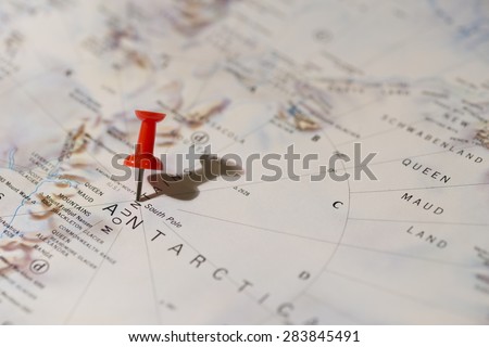 Antarctica South Pole marked on map with red pushpin. Pin casts harsh shadow to the right and is slightly angled to the right. Queen Maud Land can be seen on map.