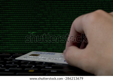 Dark computer screen with green binary code displayed with out of focus computer keyboard with male hand and credit card in foreground. Amongst the number ones and zeroes SECURITY on the screen.