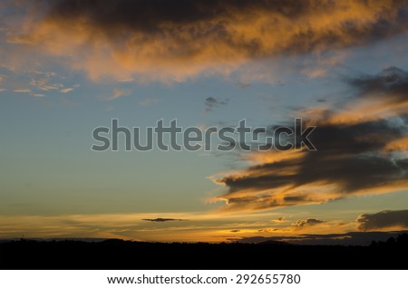 Colorful sunset landscape scene. Bottom of image shows forest silhouette on horizon. Clouds are painted to bright orange and gold by the Sun. Image taken at Queensland, Australia - Sunshine Coast.