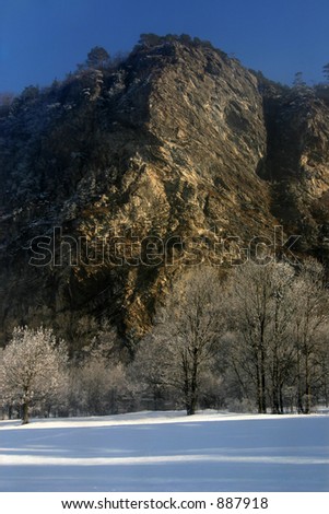 a rock face in the rising sun, snow-covered trees in the foreground.